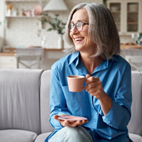 Senior woman in blue shirt smiling while drinking tea