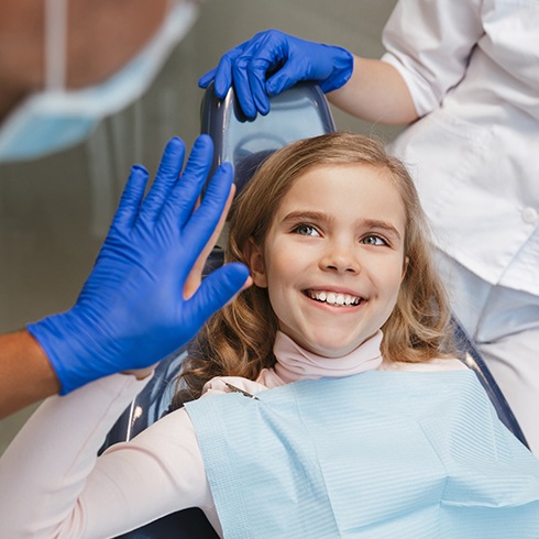 Little girl giving dentist a high five during dental checkup and teeth cleaning visit